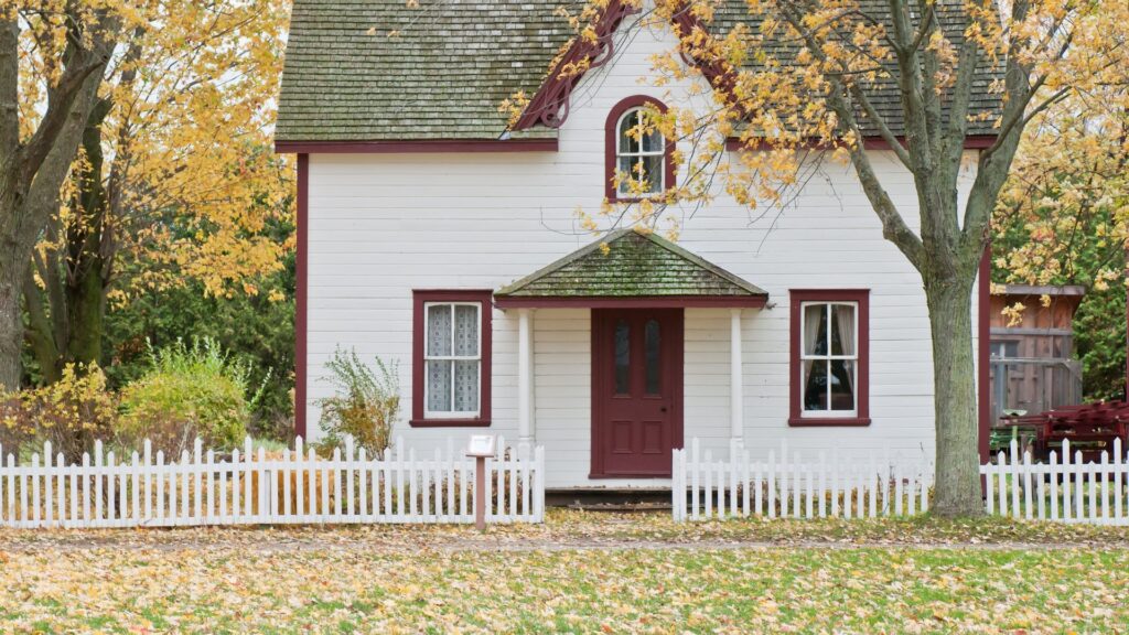 White detached house behind a picket fence with yellow autumn leaves