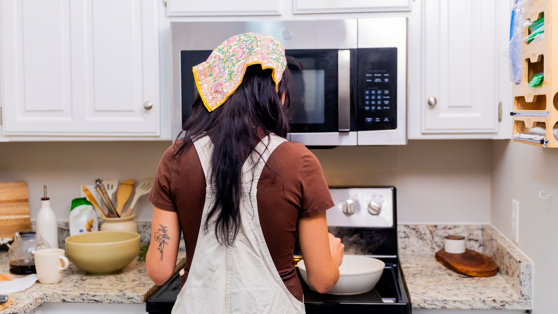 Woman seen from behind cooking at a stove in a bright white kitchen