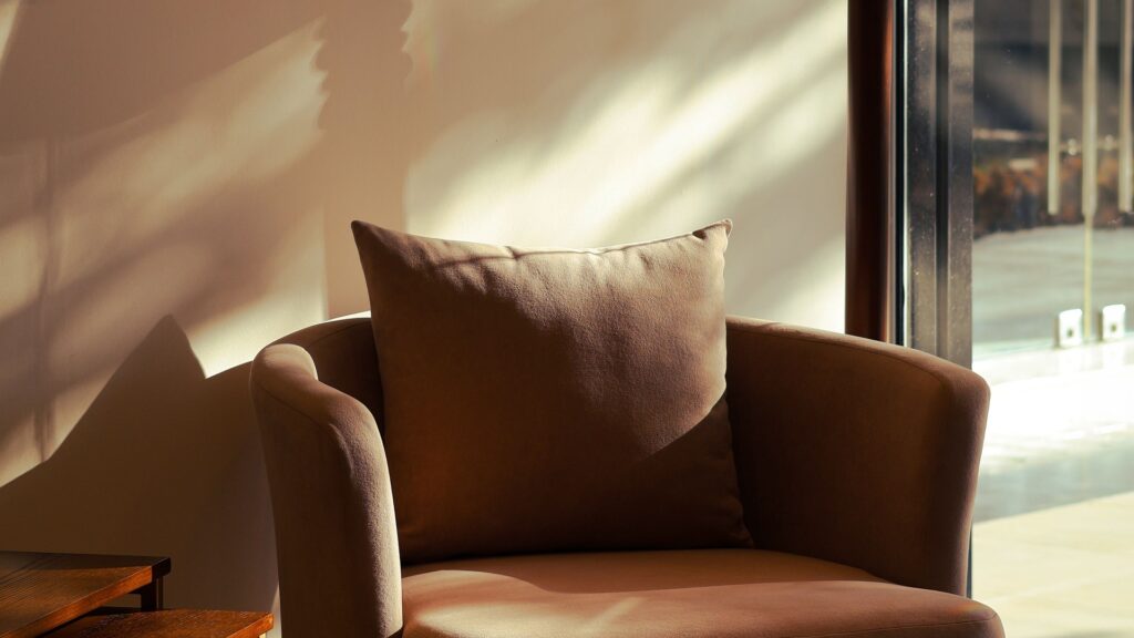 Brown armchair beside a window with afternoon sunlight casting shadows across the wall
