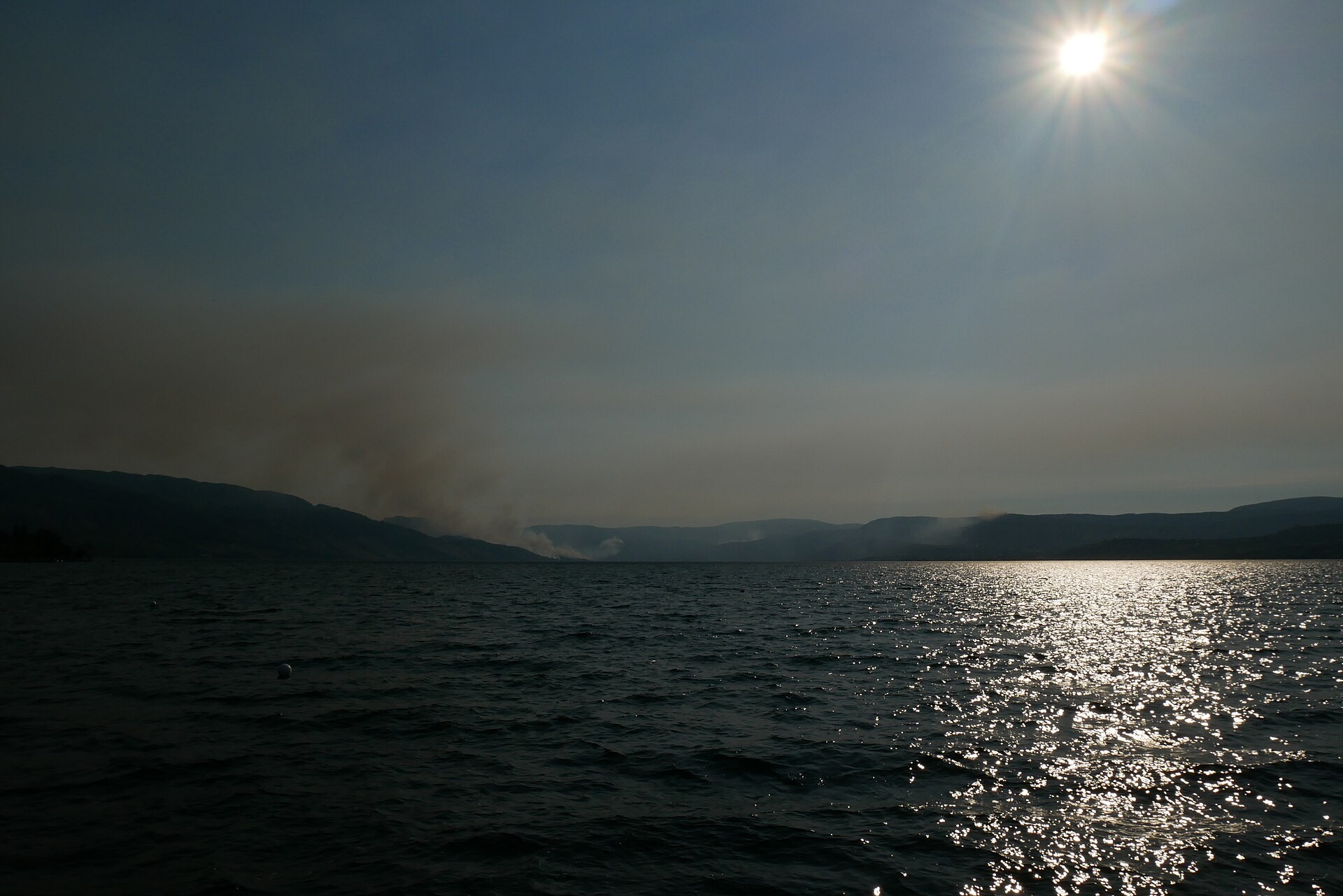 Smoke from the 2018 Mount Okanagan and Mount Eneas wildfires rising beyond Okanagan Lake under a bright afternoon sun