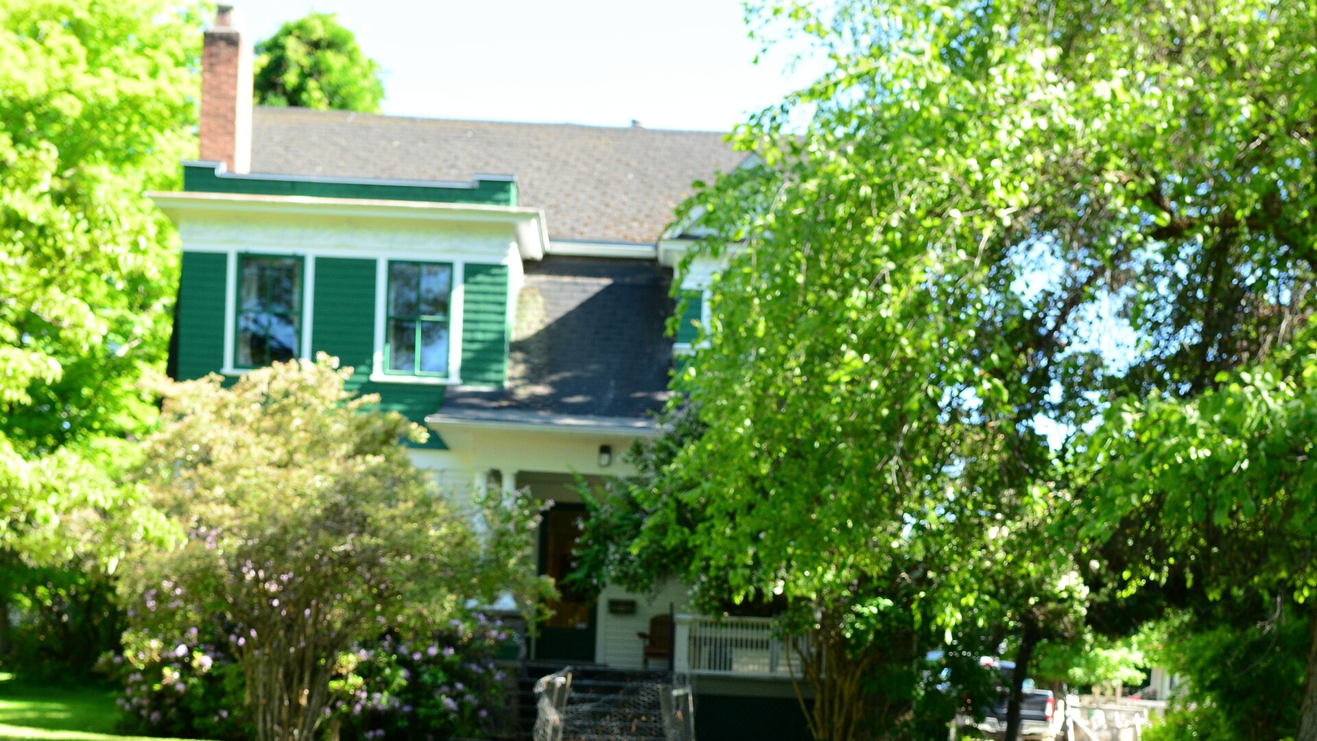 Green-and-white Gibson House behind a leafy garden in Penticton, British Columbia