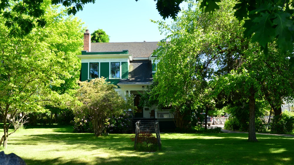 White heritage house with a covered porch and green trees in Penticton