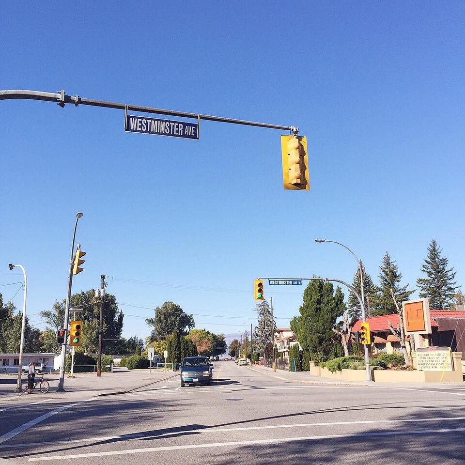 Westminster Avenue intersection in Penticton with a residential street, trees and low-rise buildings under a clear blue sky