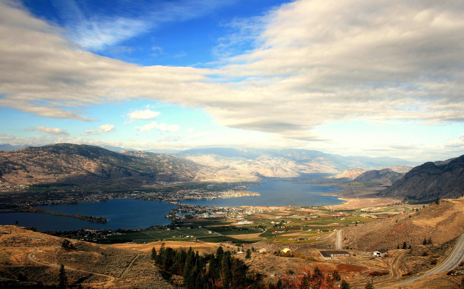 Elevated view over Osoyoos, Osoyoos Lake, surrounding hills and neighbourhoods under a partly cloudy sky
